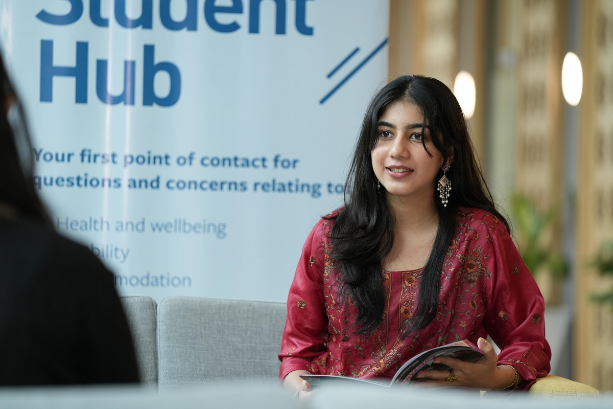 A female student in a red dress looks to a colleague across a table